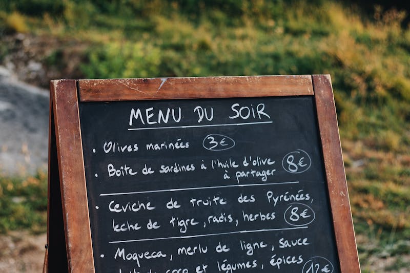 Chalkboard A-frame menu stand listing dishes and prices in outdoor restaurant setting