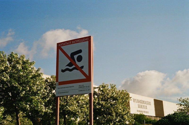 Warning sign prohibiting swimming in restricted area with trees and blue sky