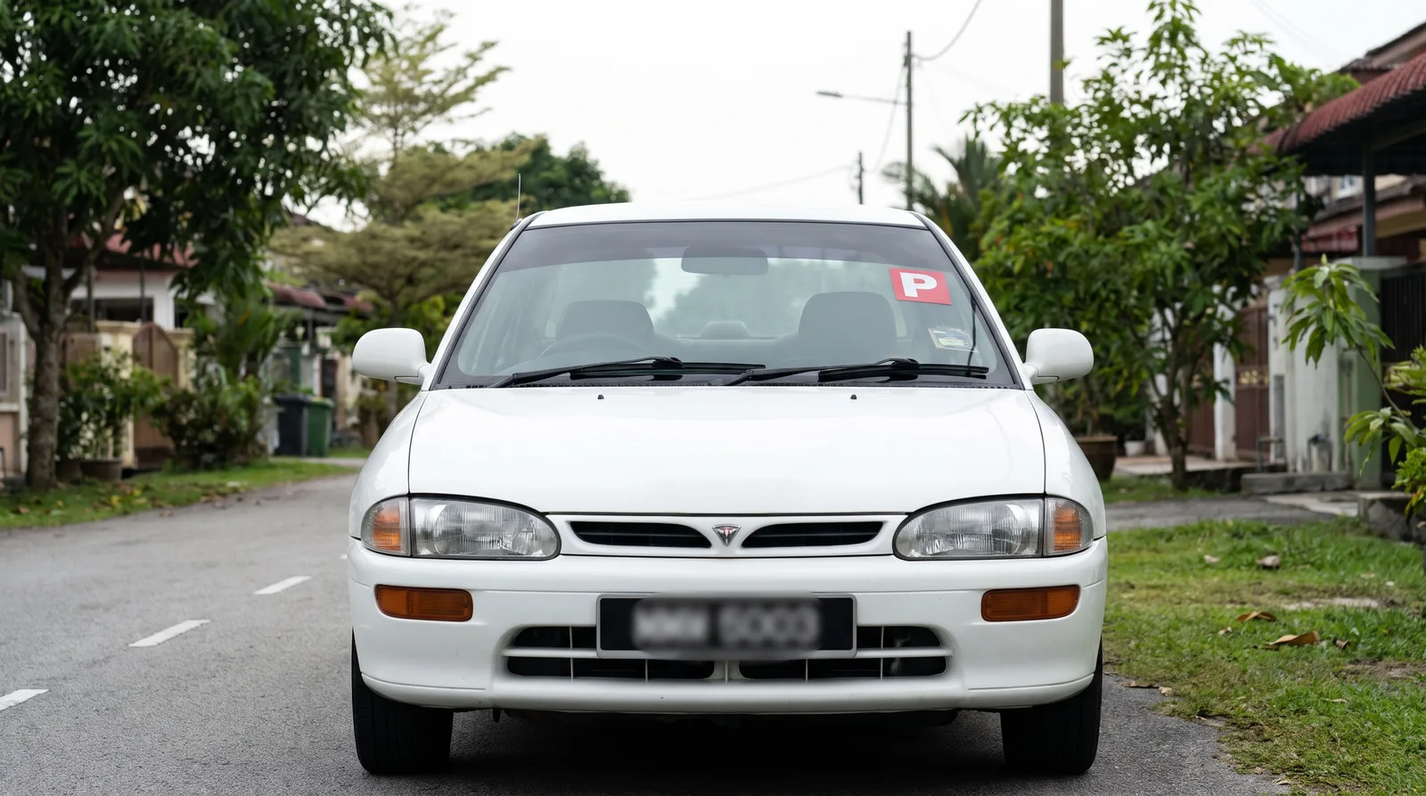 Front view of a Malaysian car showing correct P sticker placement at the top corner of the windscreen on the passenger side