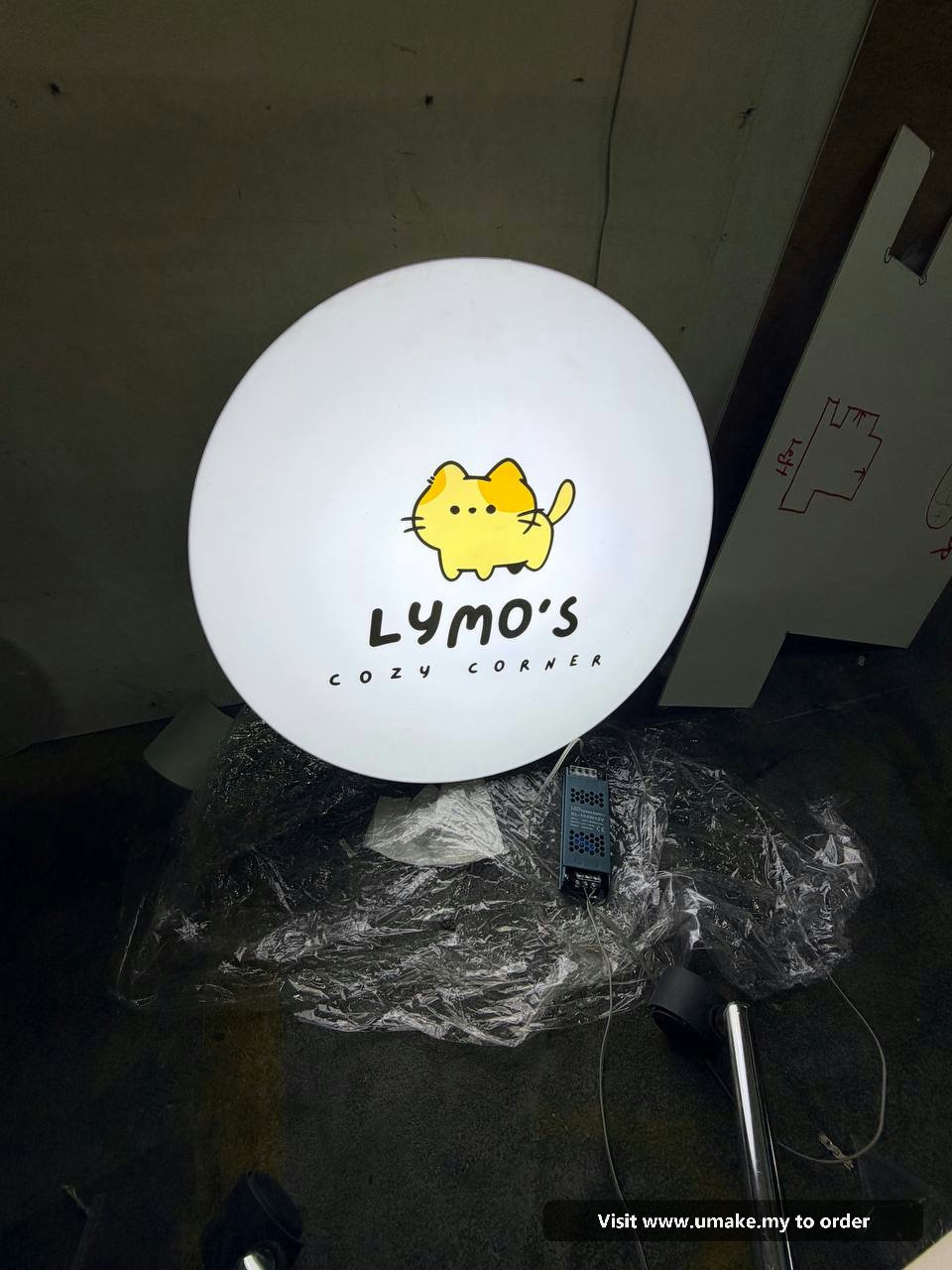 Custom Round LED Lightbox Signboard by UMAKE Malaysia (2) A round, white LED lightbox signboard for 'Lymo's Cozy Corner' featuring a cute yellow cat logo, manufactured by UMAKE Malaysia.