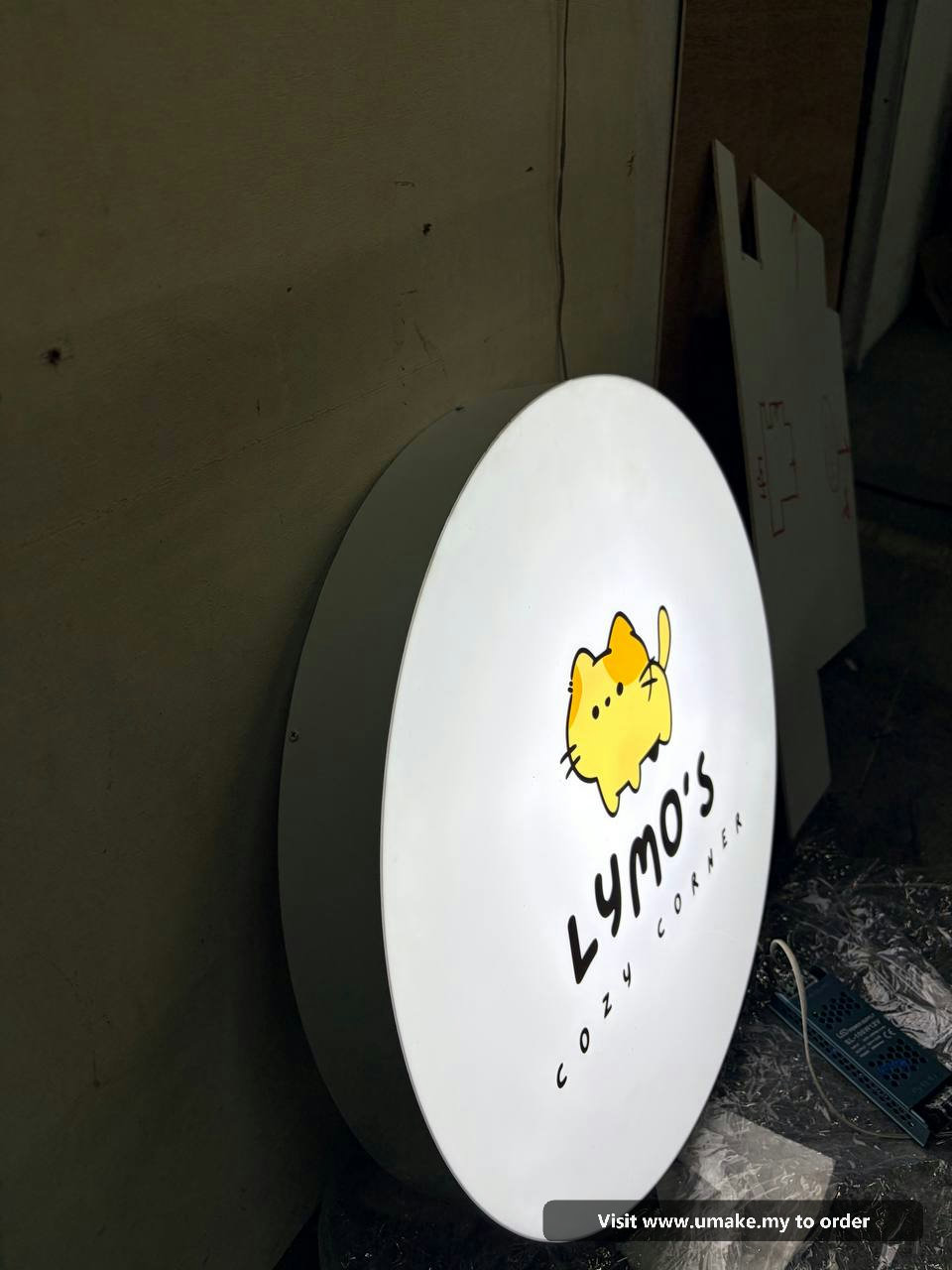 Custom Round LED Lightbox Signboard by UMAKE Malaysia (3) A round, white LED lightbox signboard for 'Lymo's Cozy Corner' featuring a cute yellow cat logo, manufactured by UMAKE Malaysia.