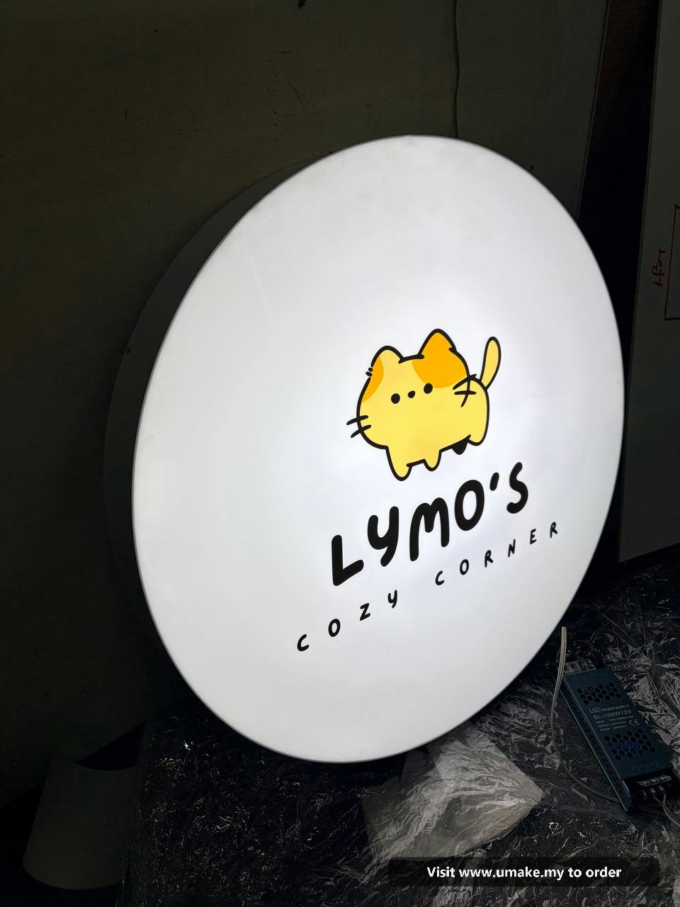 Custom Round LED Lightbox Signboard by UMAKE Malaysia (4) A round, white LED lightbox signboard for 'Lymo's Cozy Corner' featuring a cute yellow cat logo, manufactured by UMAKE Malaysia.