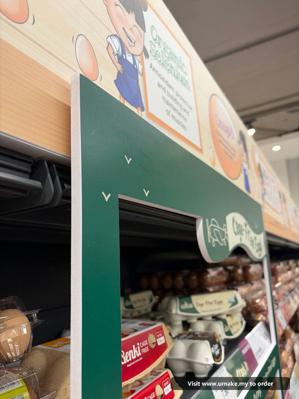 Custom PVC Signage with Sticker Printing by UMAKE Malaysia (2) A custom-cut green PVC signage with 'Cage-Free Eggs' text and graphics, featuring a plane and chickens, installed in a supermarket aisle above egg car