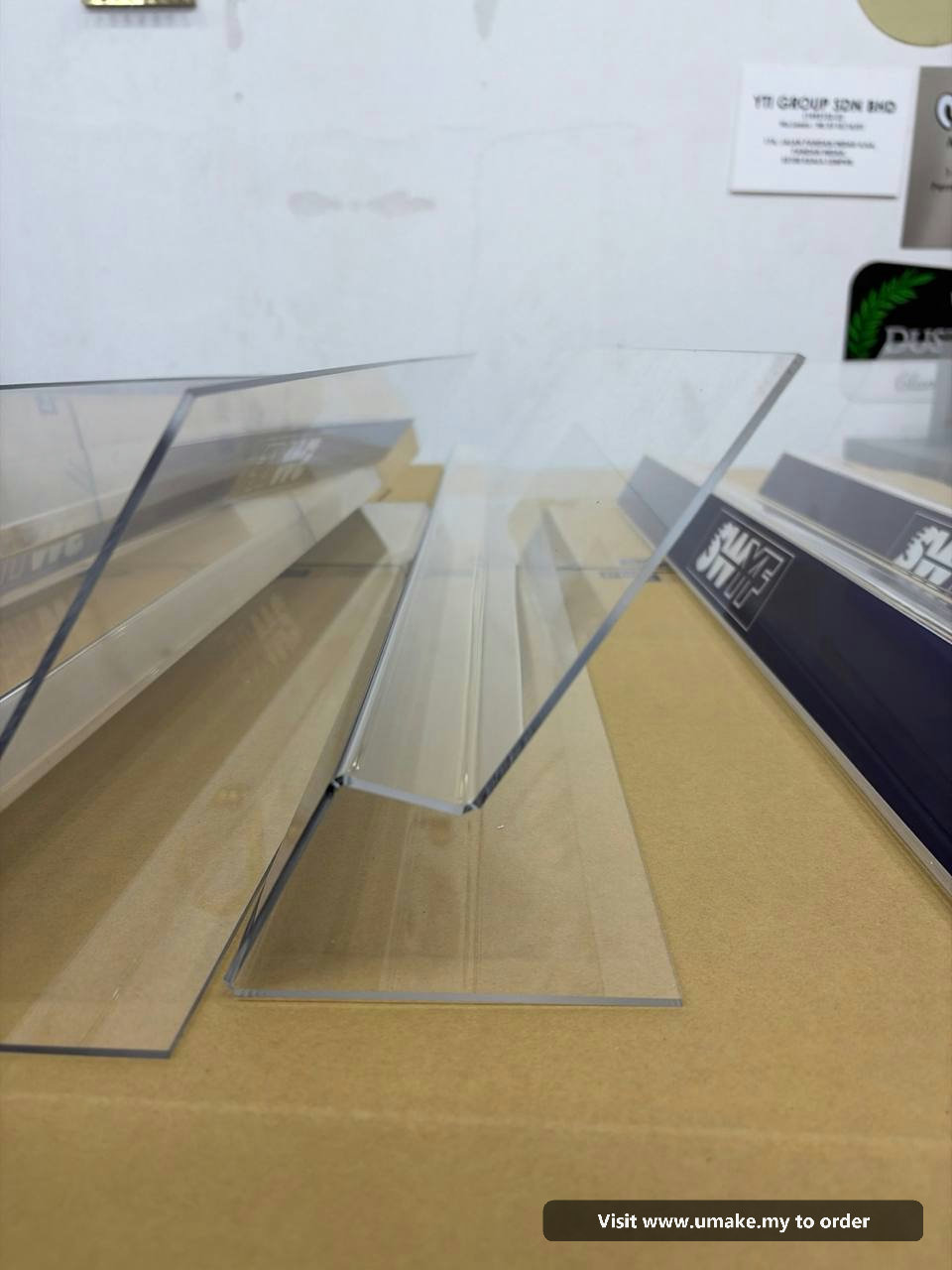 Custom Acrylic Display Stands by UMAKE Malaysia (3) Several clear acrylic display stands with dark blue bases, featuring the white 'SWYF' logo, laid out on a cardboard surface in a manufacturing facilit