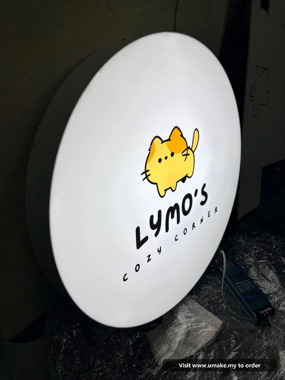 Custom Round LED Lightbox Signboard by UMAKE Malaysia A round, white LED lightbox signboard for 'Lymo's Cozy Corner' featuring a cute yellow cat logo, manufactured by UMAKE Malaysia.