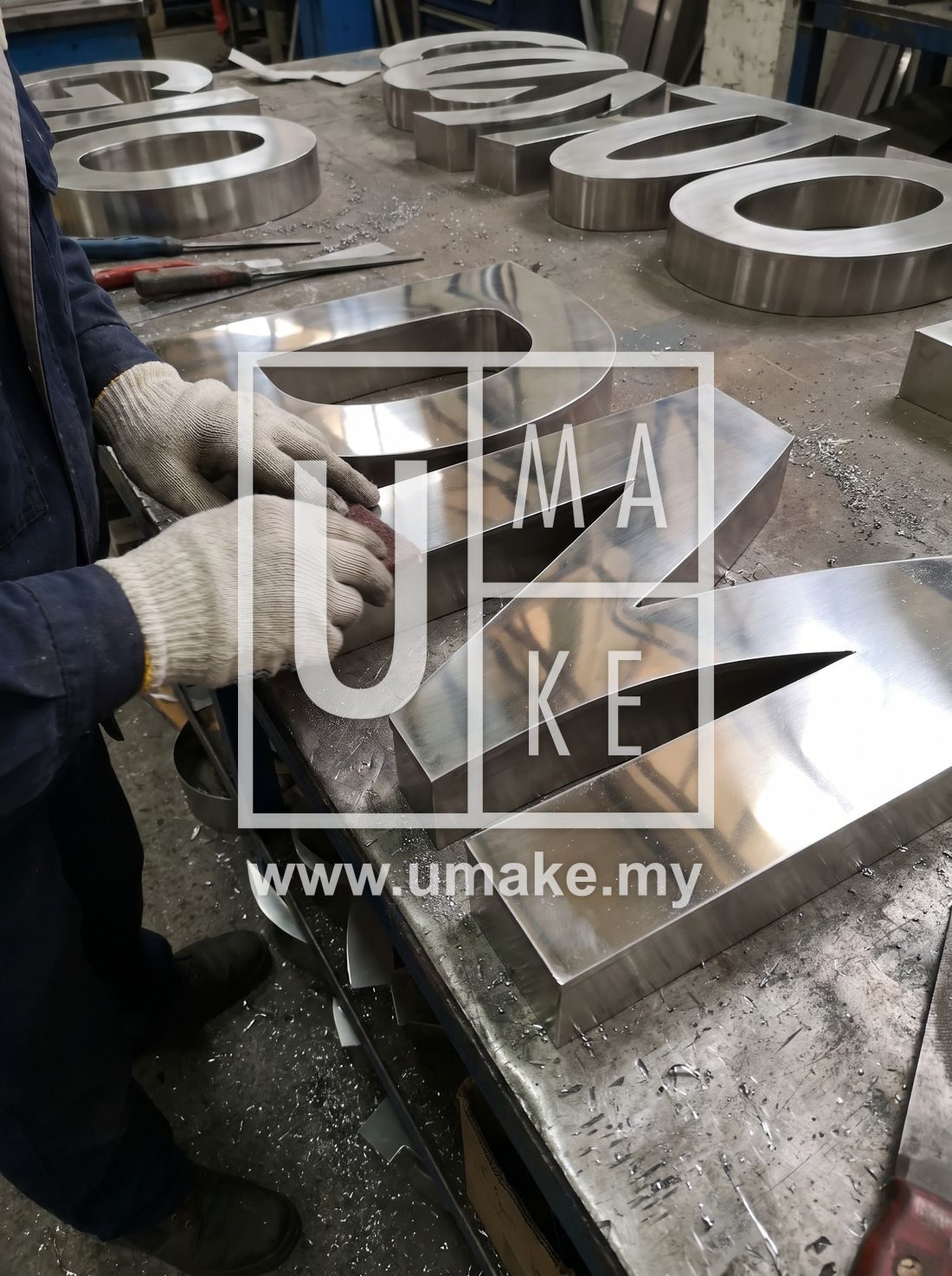 Close-up of polished stainless steel channel letters being hand-finished in a factory